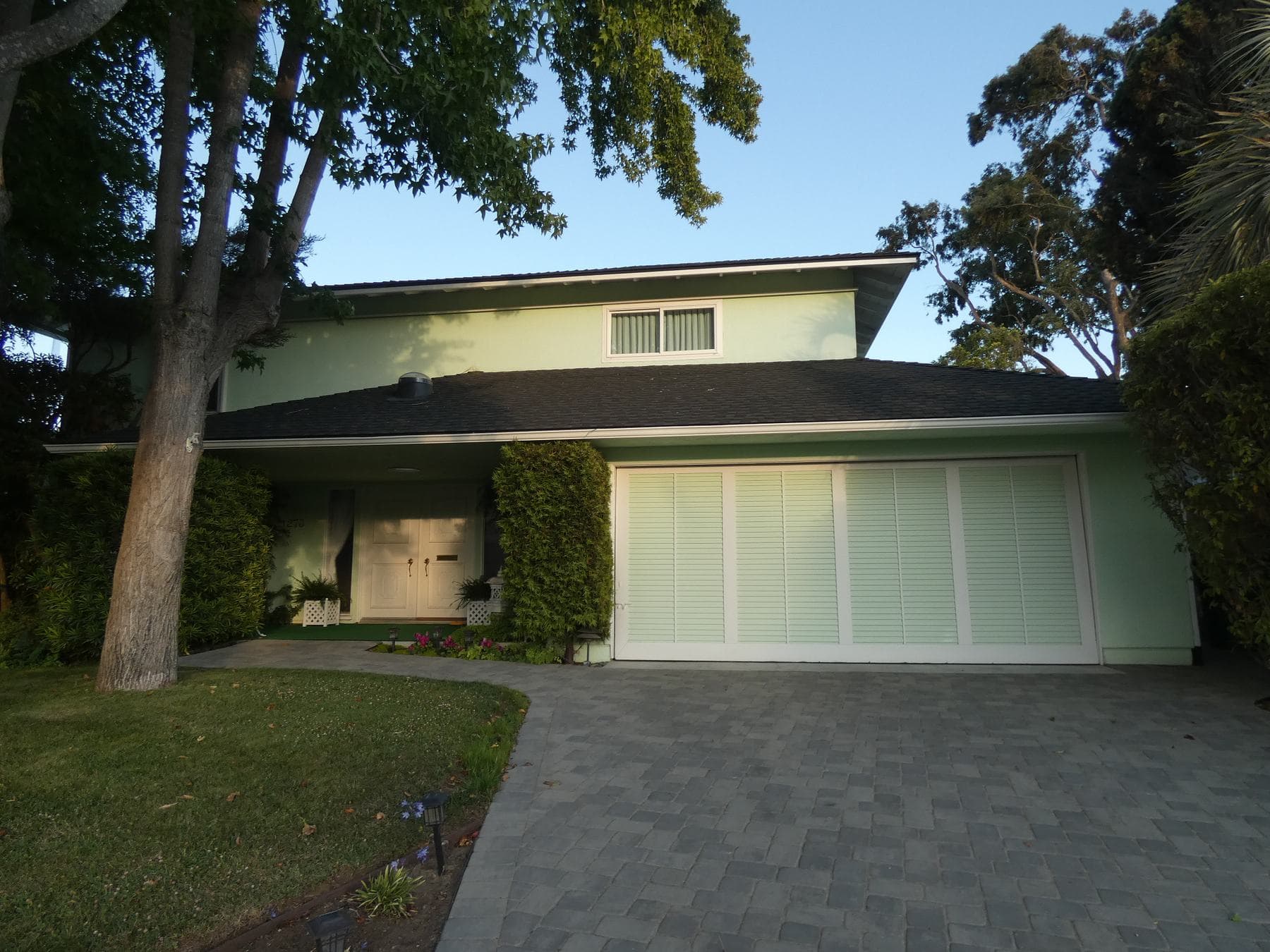 A two-storey house with a wide paved driveway leading to a double garage, framed by trees and a lawn